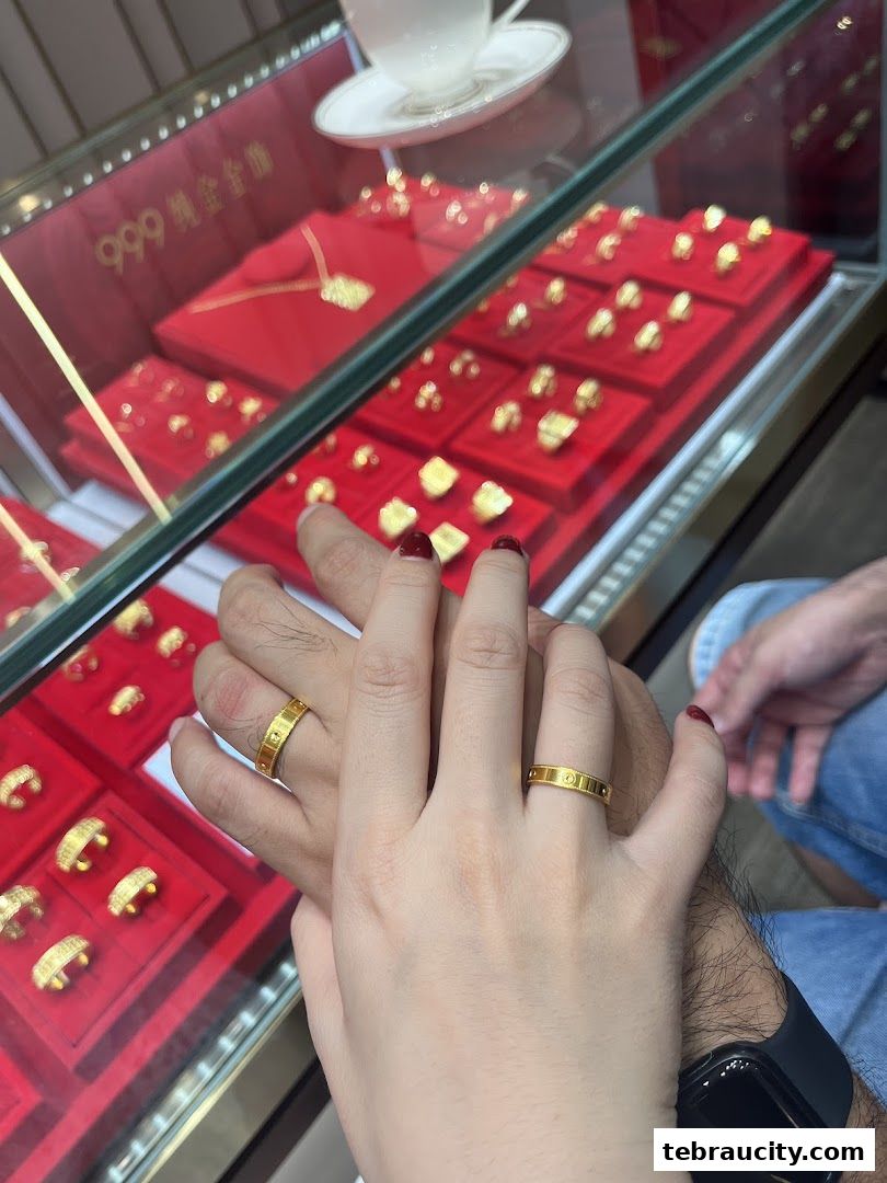 Couple's hands wearing gold rings in front of a jewelry display case.