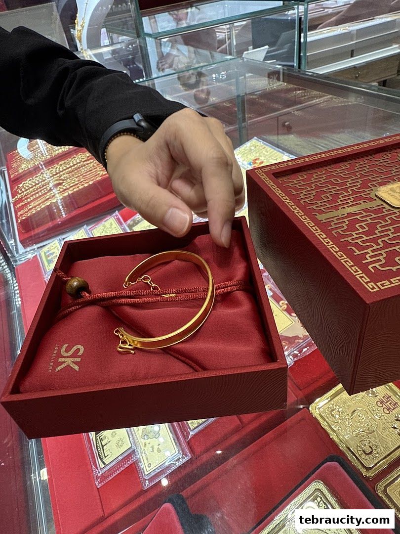 A hand is shown presenting a gold bracelet from a red jewelry box at SK Jewellery.