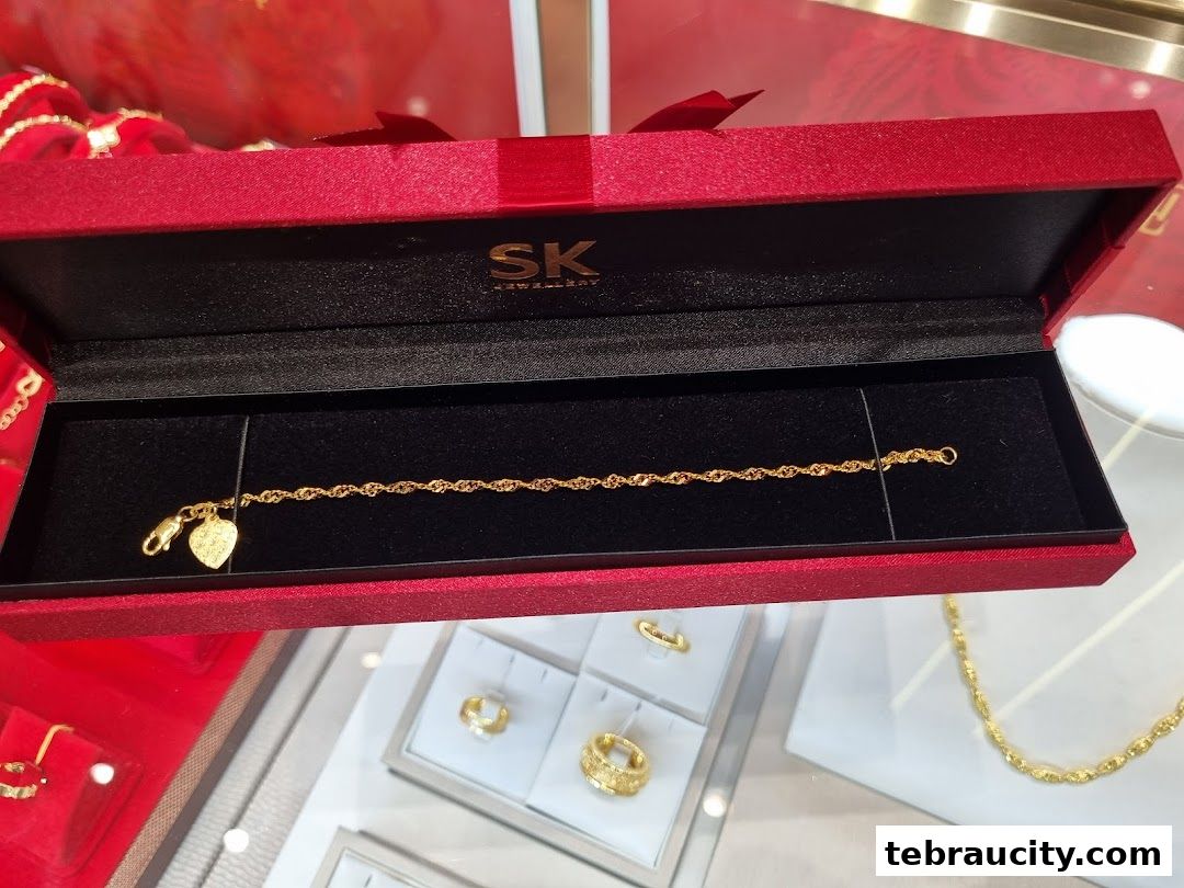 A gold bracelet with a heart charm displayed in a red jewelry box.
