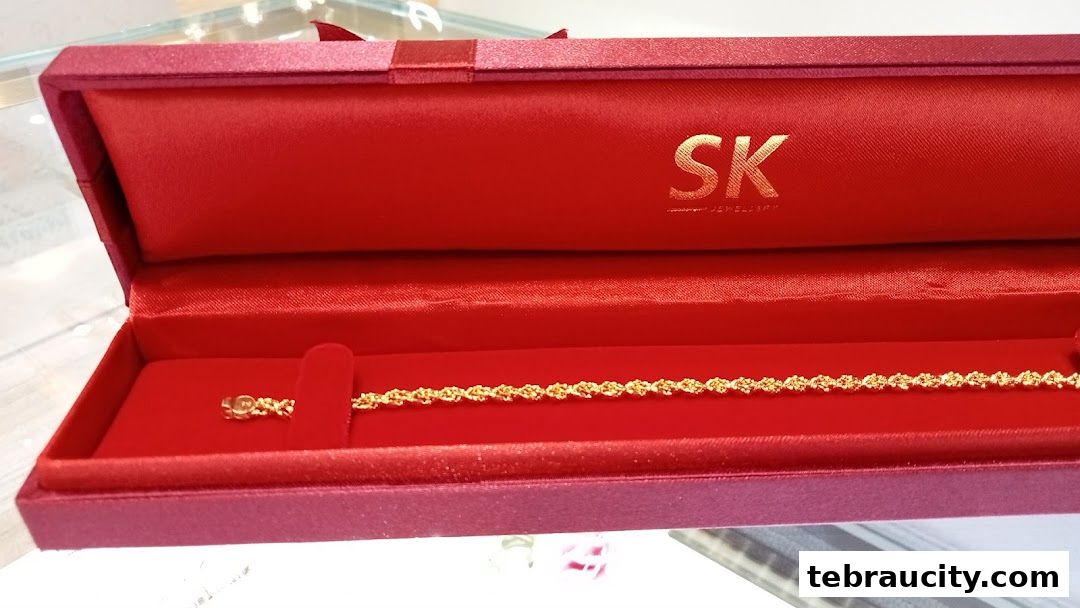 A gold bracelet displayed in a red jewelry box with the SK Jewellery logo.