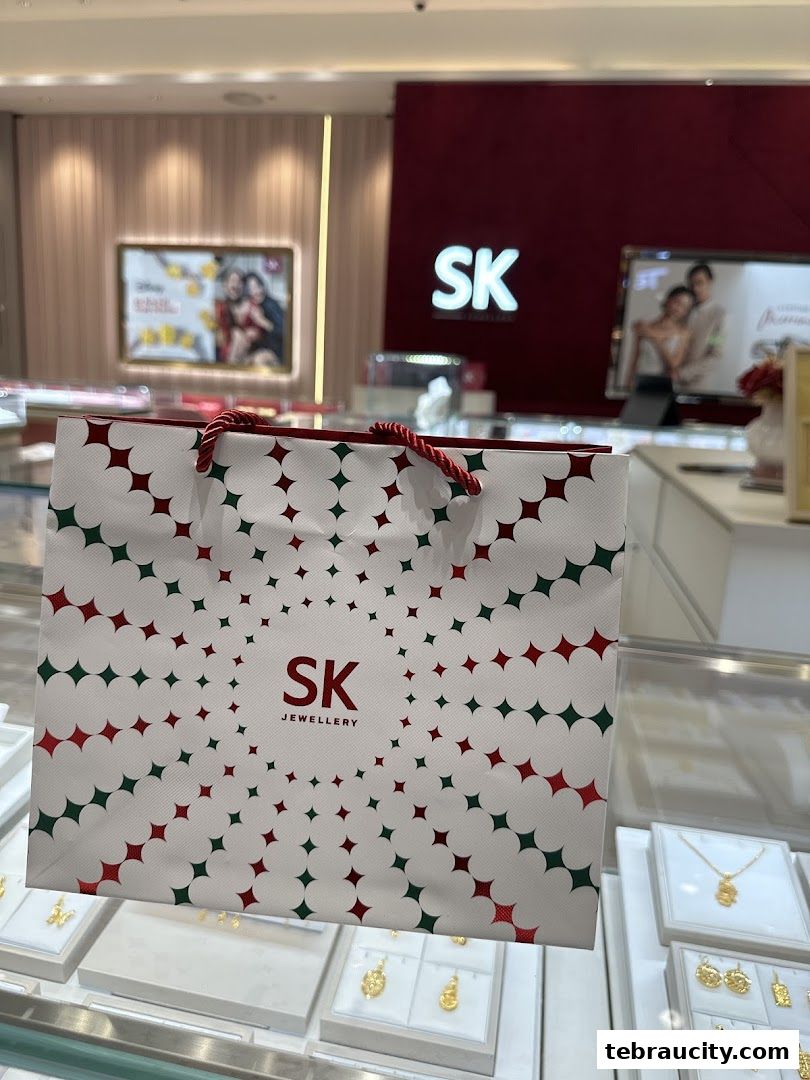 A shopping bag from SK Jewellery with a festive pattern in front of a display of gold jewelry.