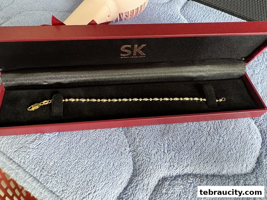 A gold and silver beaded bracelet displayed in a red SK Jewellery box.
