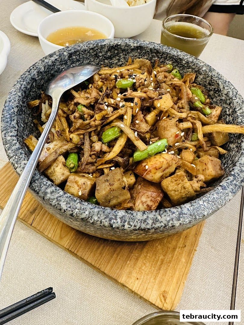 A stone bowl filled with a savory dish of mushrooms, tofu, and green beans, served with a side of soup.