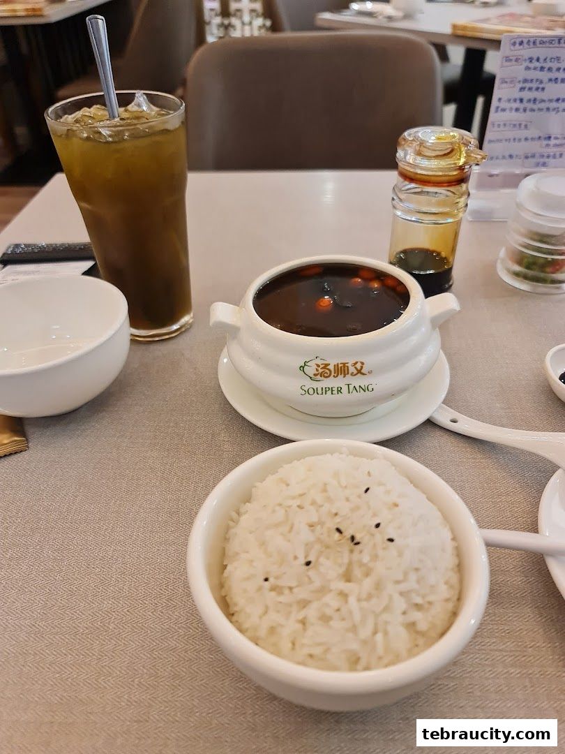 A bowl of soup, a glass of iced tea, and a bowl of rice are served on a table.