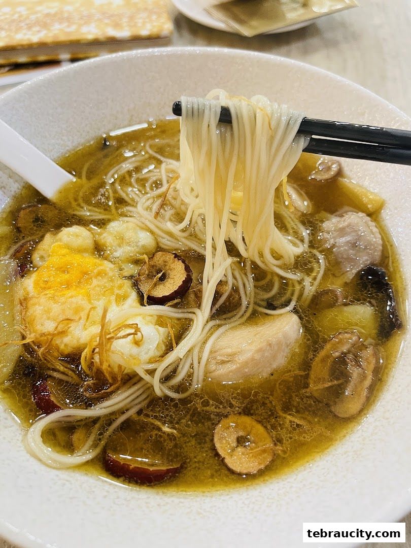 A close-up shot of a steaming bowl of noodle soup with chicken, egg, and herbs.