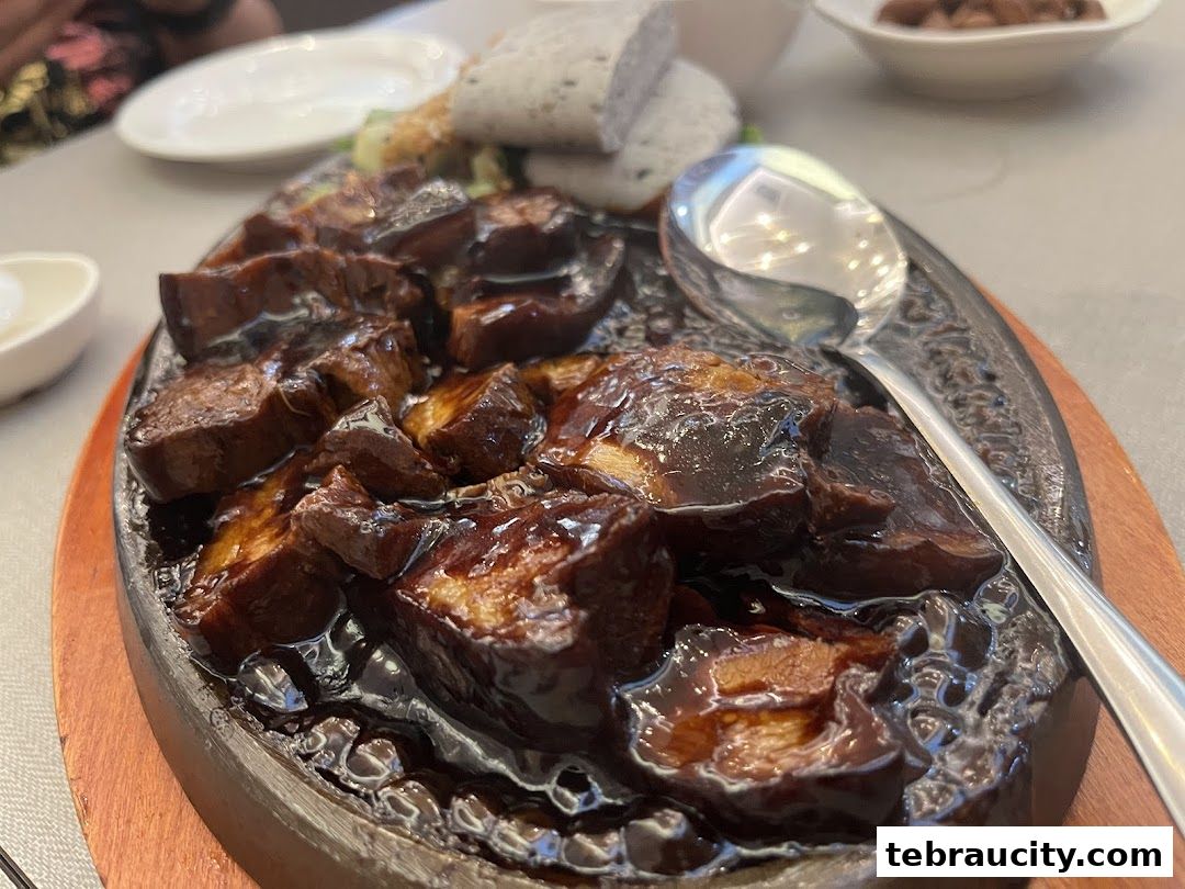 A close-up shot of a sizzling dish with glazed meat and a spoon on a hot plate.