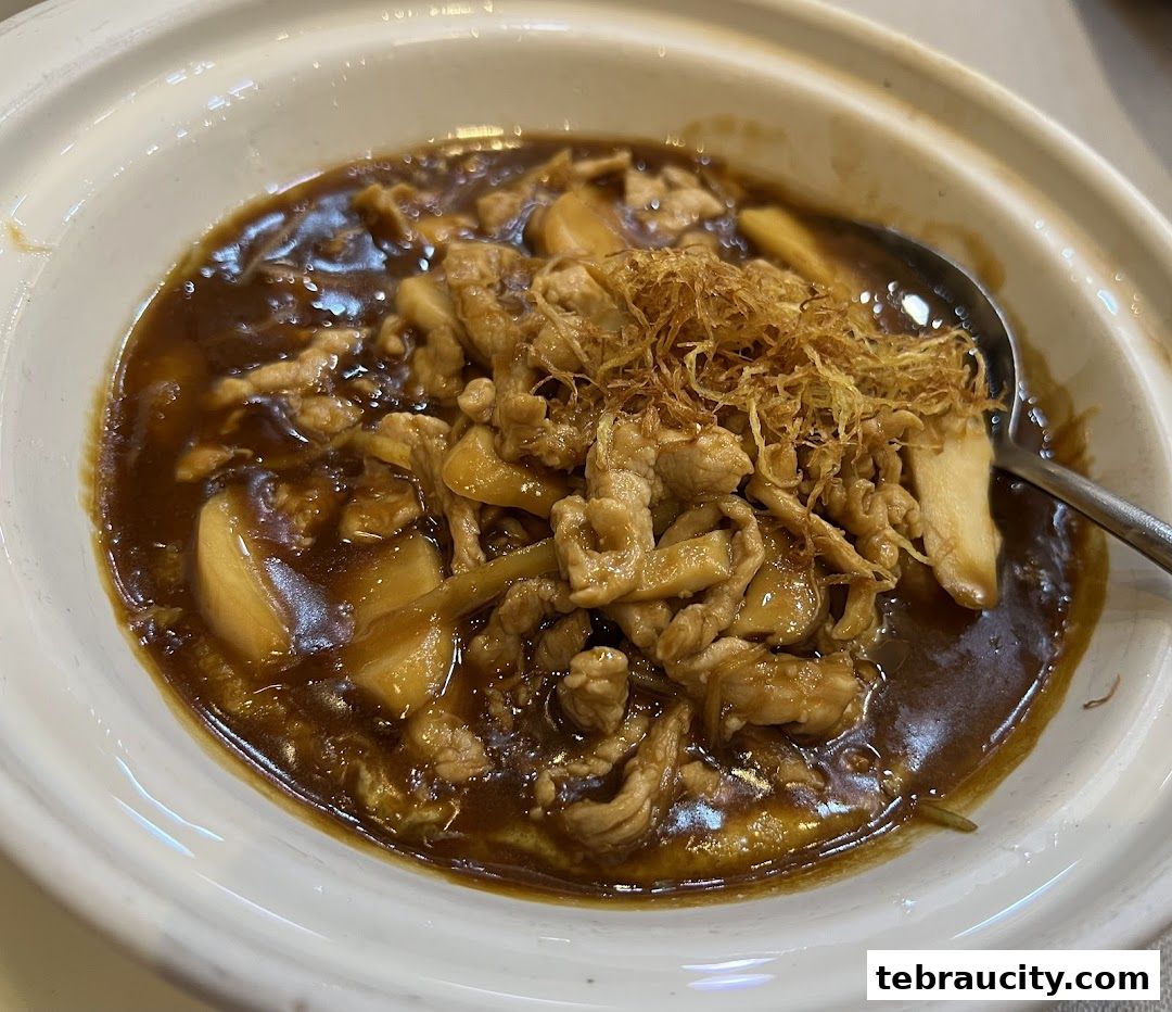A close-up shot of a delicious dish with sliced meat, mushrooms, and crispy fried shallots in a savory sauce.