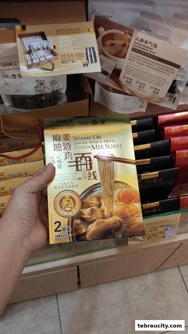 A hand holds a box of Souper Tang Sesame Oil Chicken Mee Suah, with other soup products in the background.