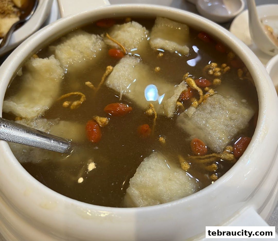 A close-up shot of a steaming bowl of soup with various ingredients like goji berries and herbs.