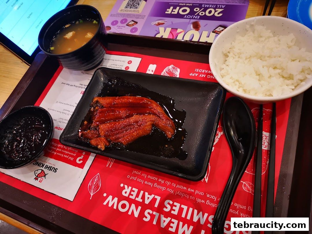A tray of Japanese food including grilled eel, rice, miso soup, and a side dish.