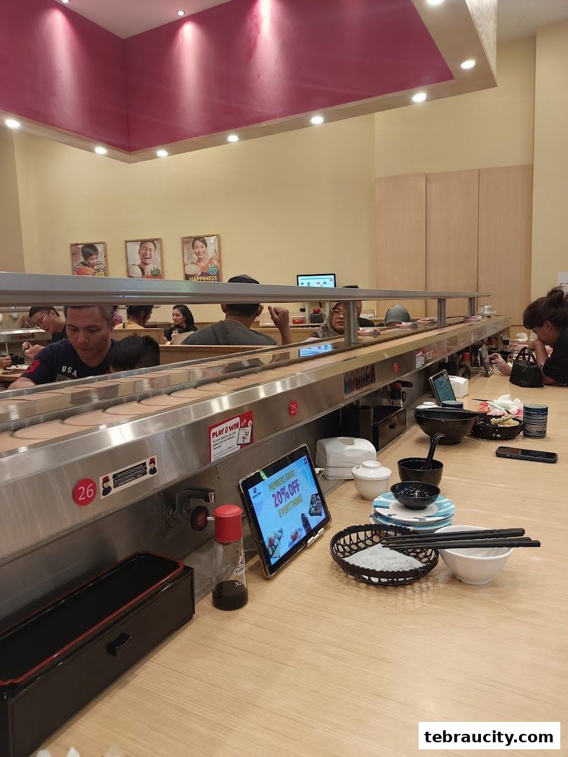 Diners enjoy sushi at a conveyor belt restaurant with digital ordering tablets.