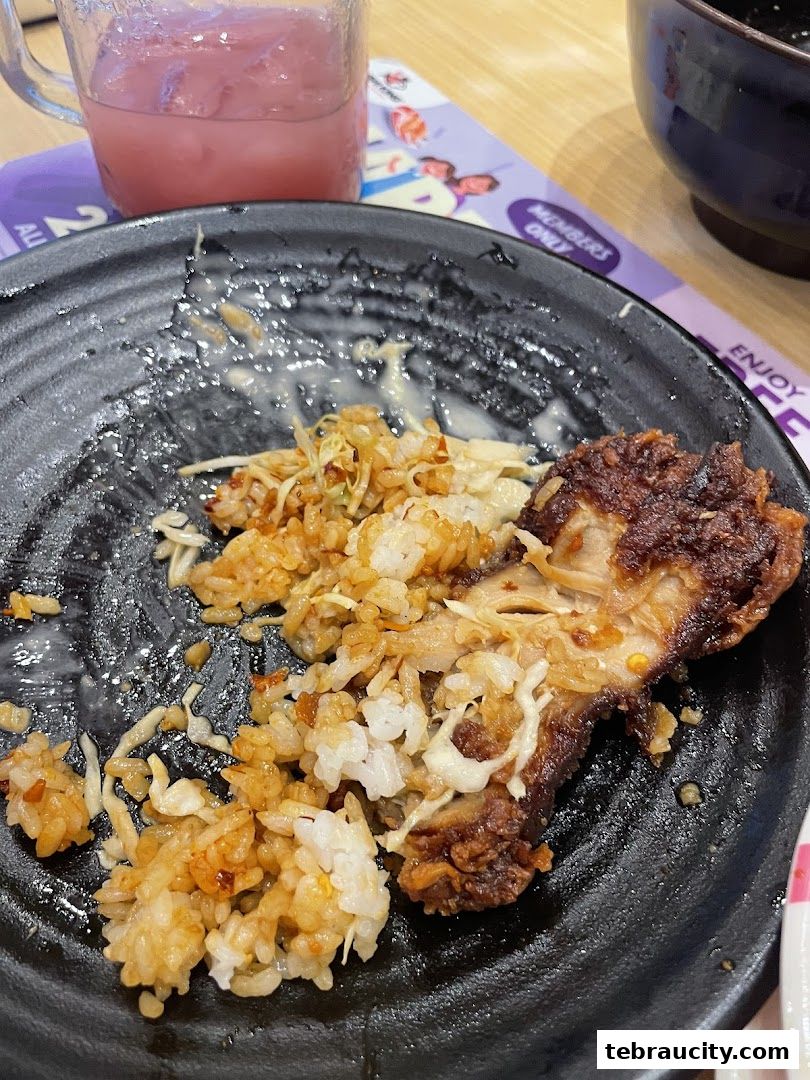 A close-up of a nearly finished plate of Japanese fried rice with a piece of meat and a pink drink.