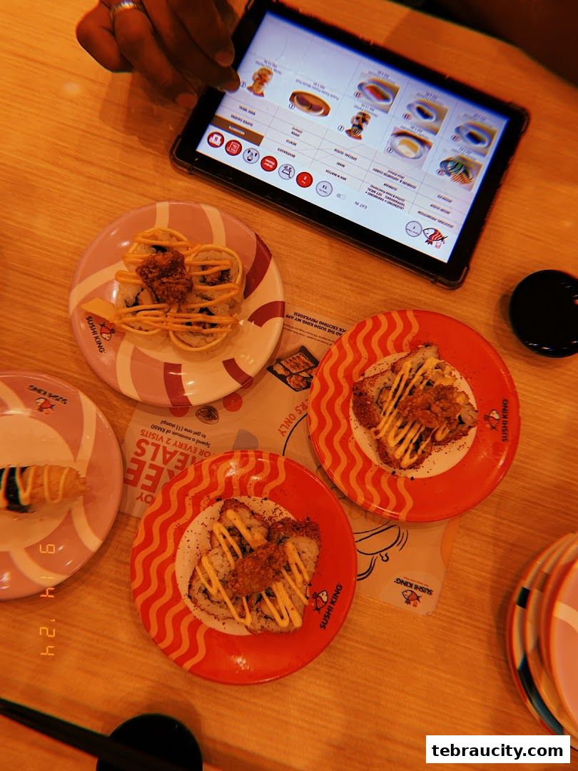 Plates of sushi and a tablet displaying a menu on a wooden table.
