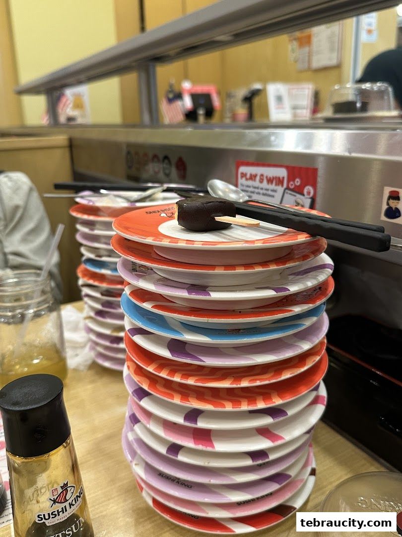 Stacks of colorful sushi plates and a bottle of soy sauce on a table.