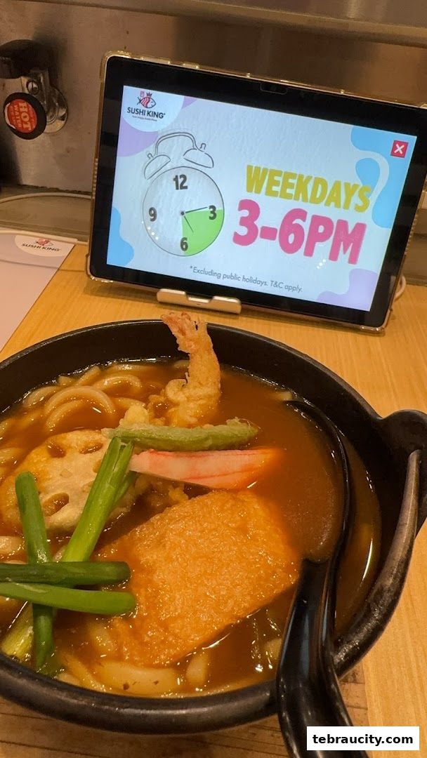 A bowl of Japanese curry udon with tempura shrimp and other toppings, next to a tablet displaying a promotion.