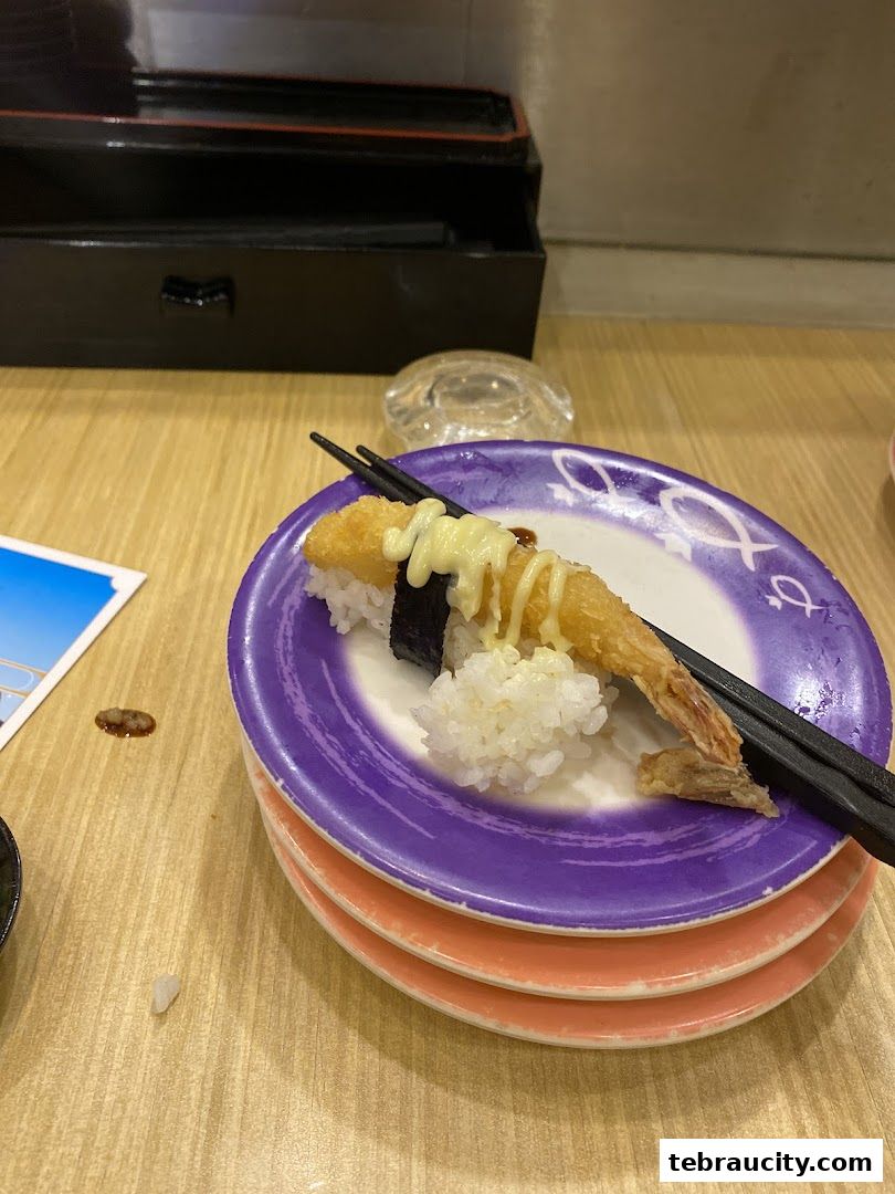 A plate of sushi with a fried shrimp, rice, and seaweed, topped with mayonnaise.