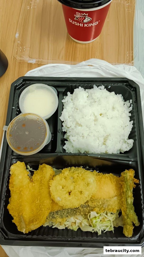 A bento box with fried fish, rice, and dipping sauces, alongside a Sushi King branded cup.