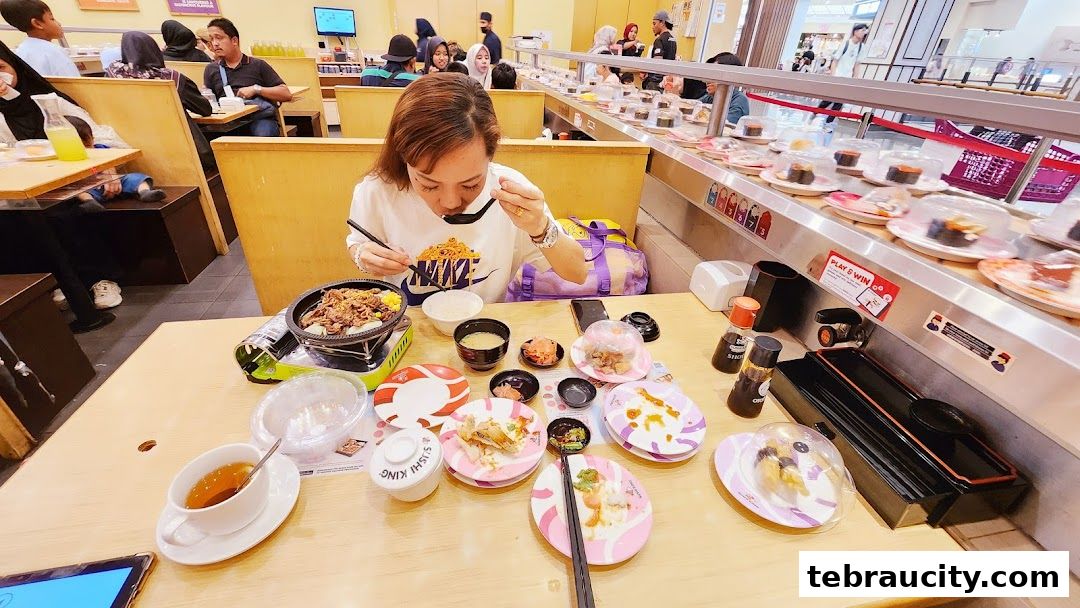 A woman enjoys a meal at Sushi King, with a conveyor belt of sushi in the background.