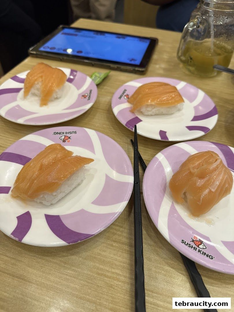 Plates of salmon sushi served on a table with chopsticks and a tablet.