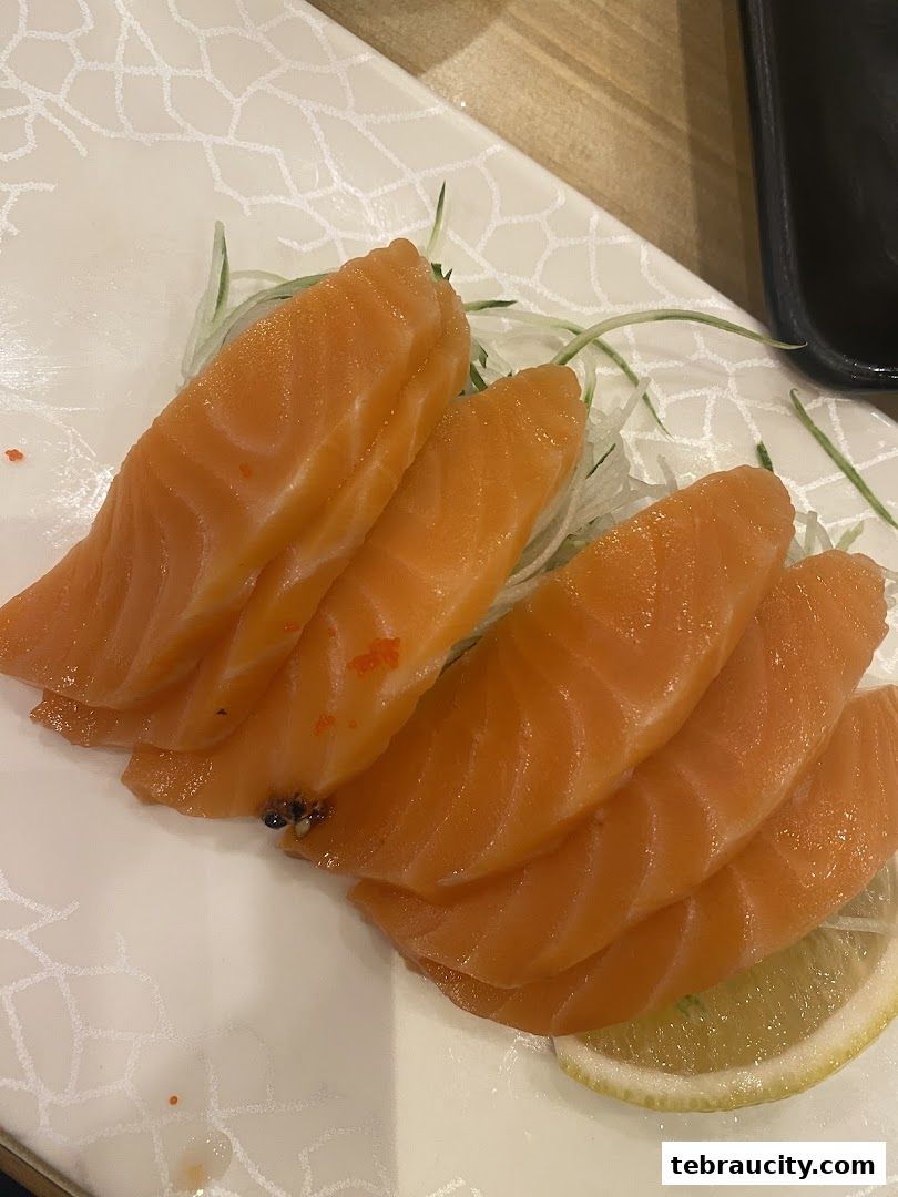 Fresh salmon sashimi served on a white plate with shredded daikon and a lemon slice.