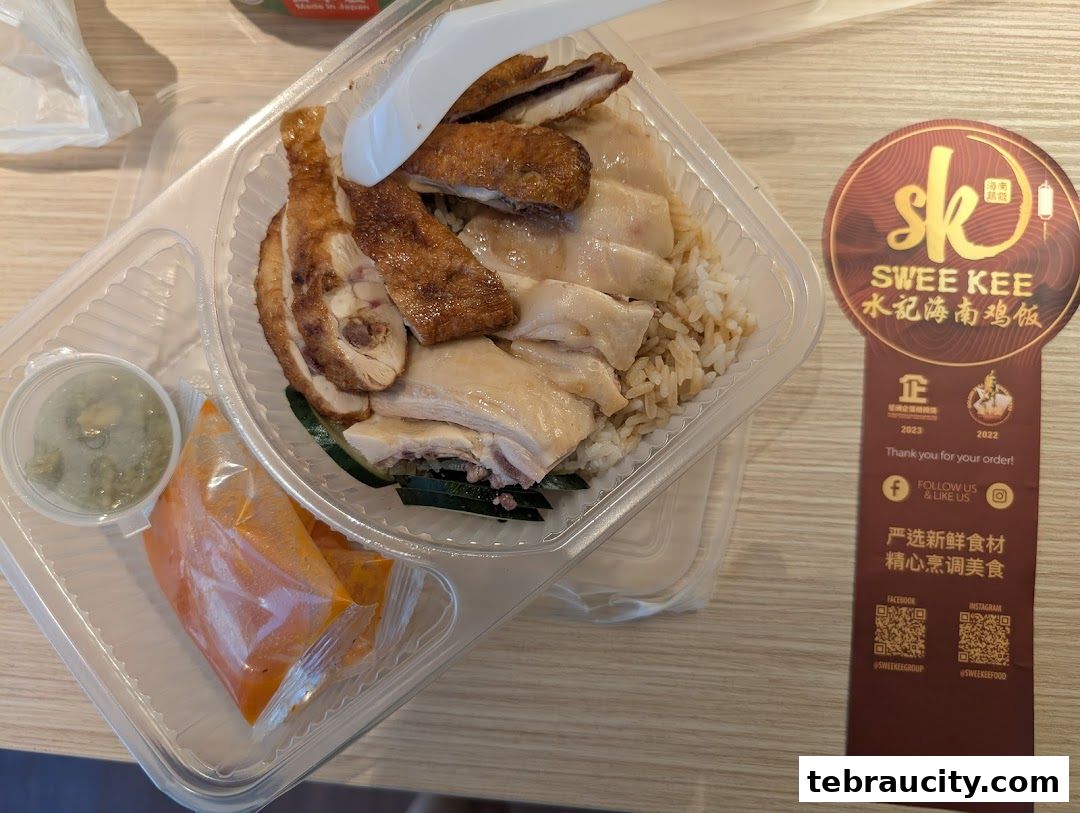 A takeaway container of chicken rice with dipping sauces and a branded sticker.