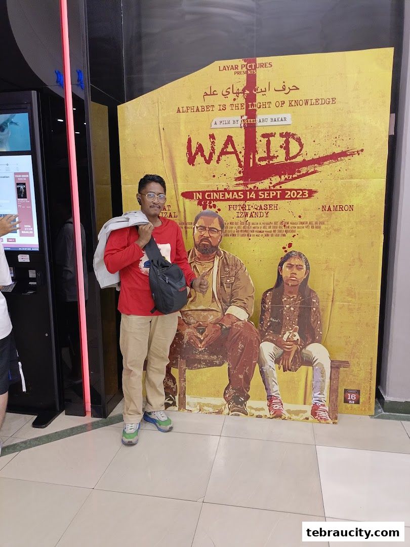 A man poses in front of a movie poster for 'Wa'id' at a cinema.