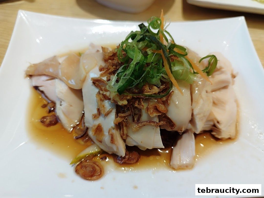 A plate of succulent steamed chicken with soy sauce, fried shallots, and spring onions.