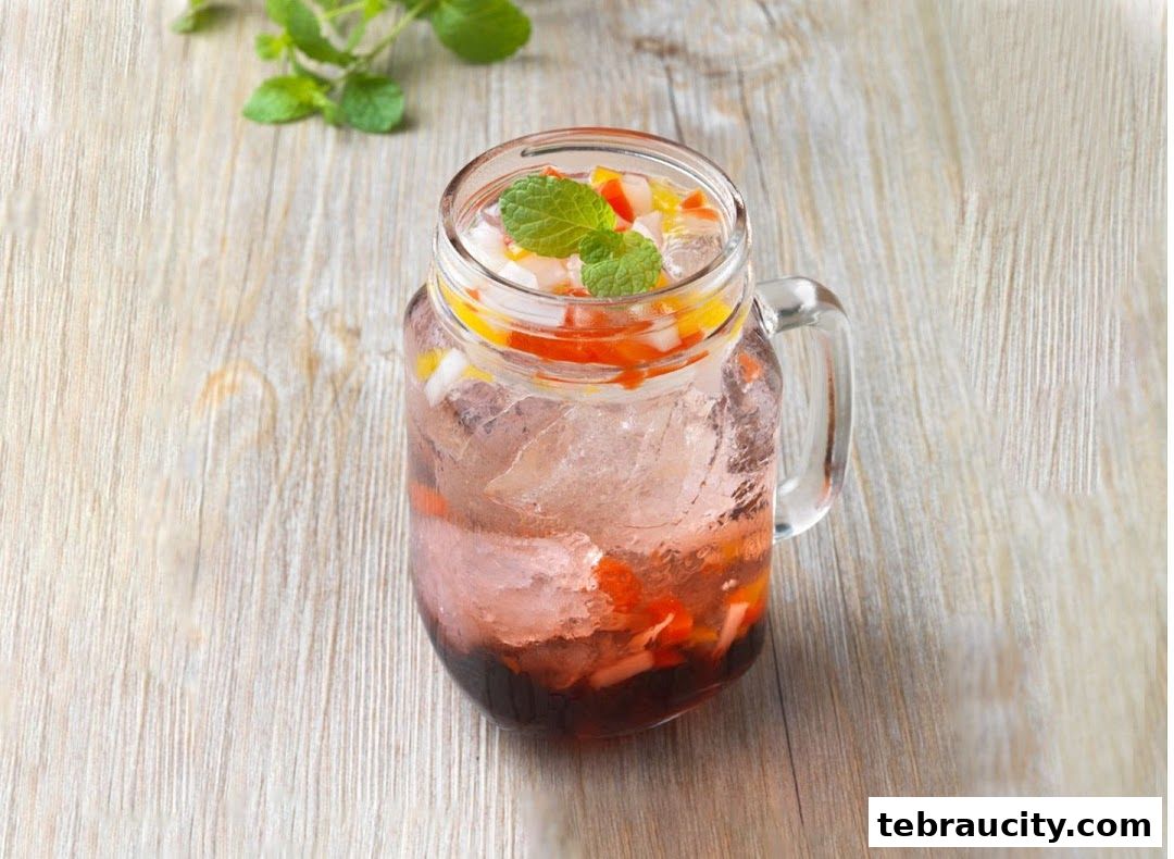 A refreshing glass of iced fruit drink with mint leaves on a wooden table.