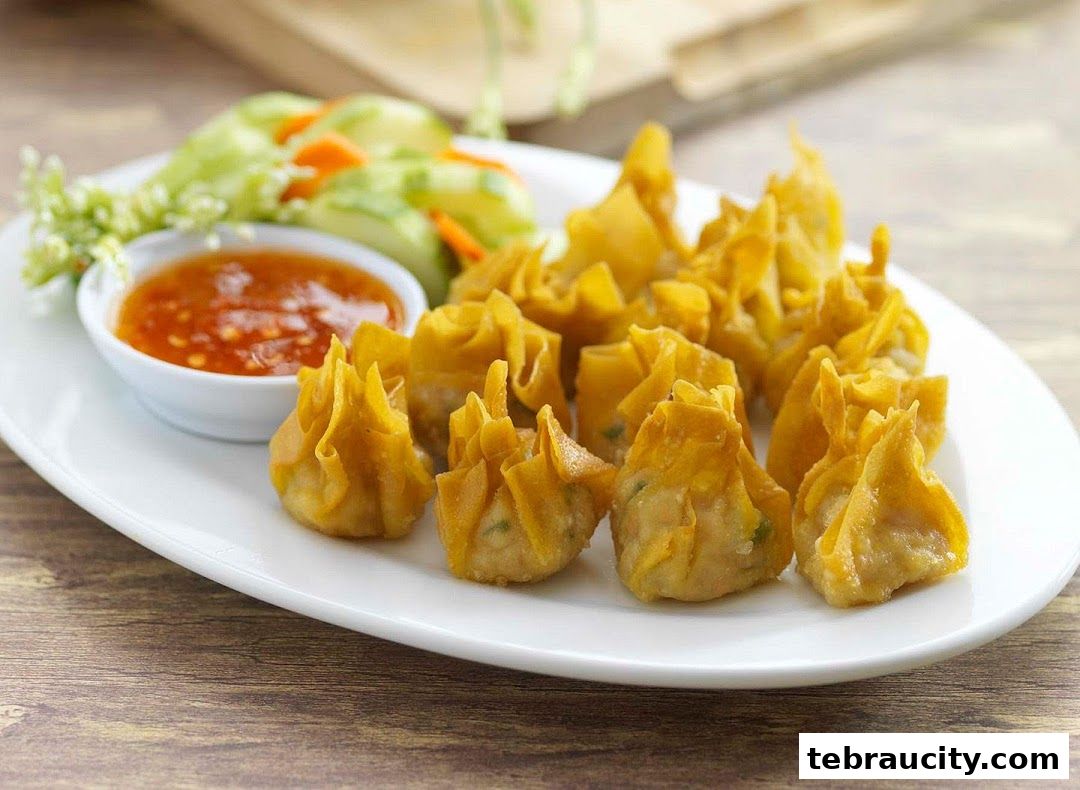 A plate of golden fried wontons served with a side of sweet chili sauce and cucumber salad.