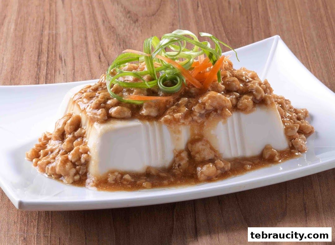 A close-up of a white tofu dish topped with minced meat and garnished with scallions and carrots.