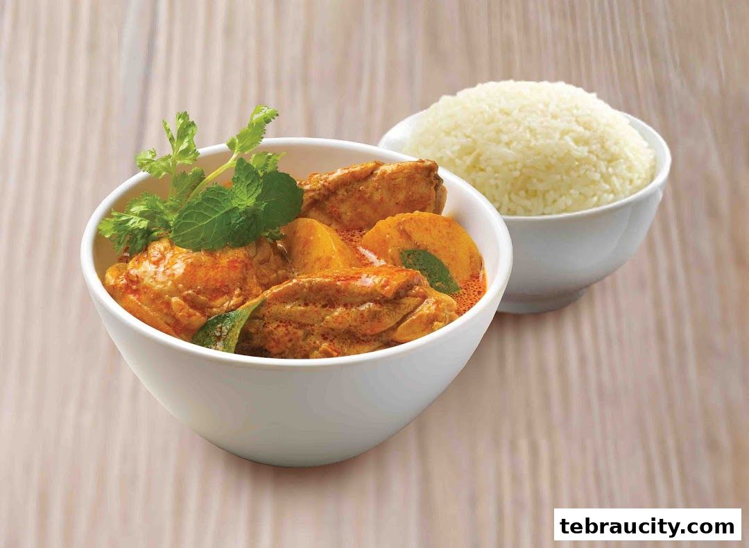 A bowl of chicken curry with potatoes and rice, garnished with fresh herbs.