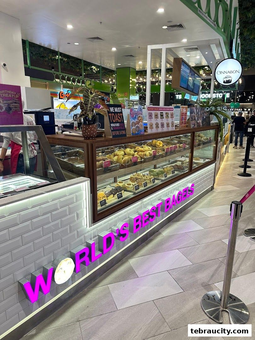 A bakery display case filled with various bagels and cinnamon rolls, with prominent signage.