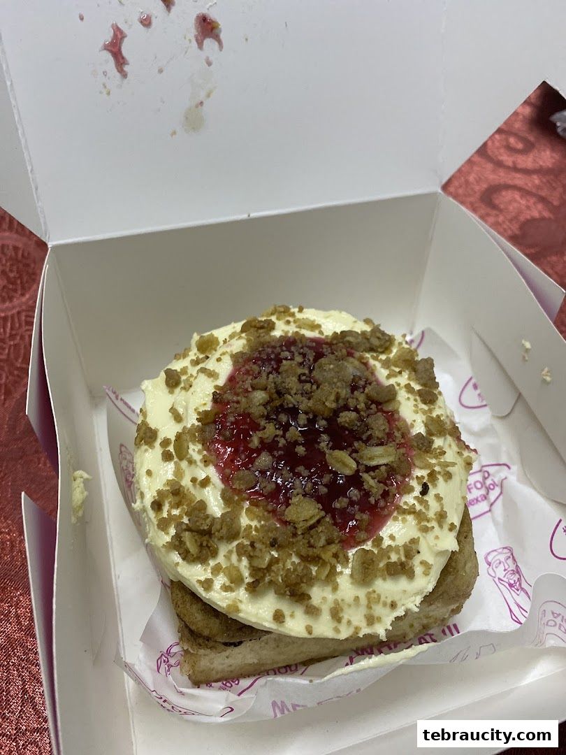A close-up of a delicious pastry with cream cheese frosting and berry topping in a white box.