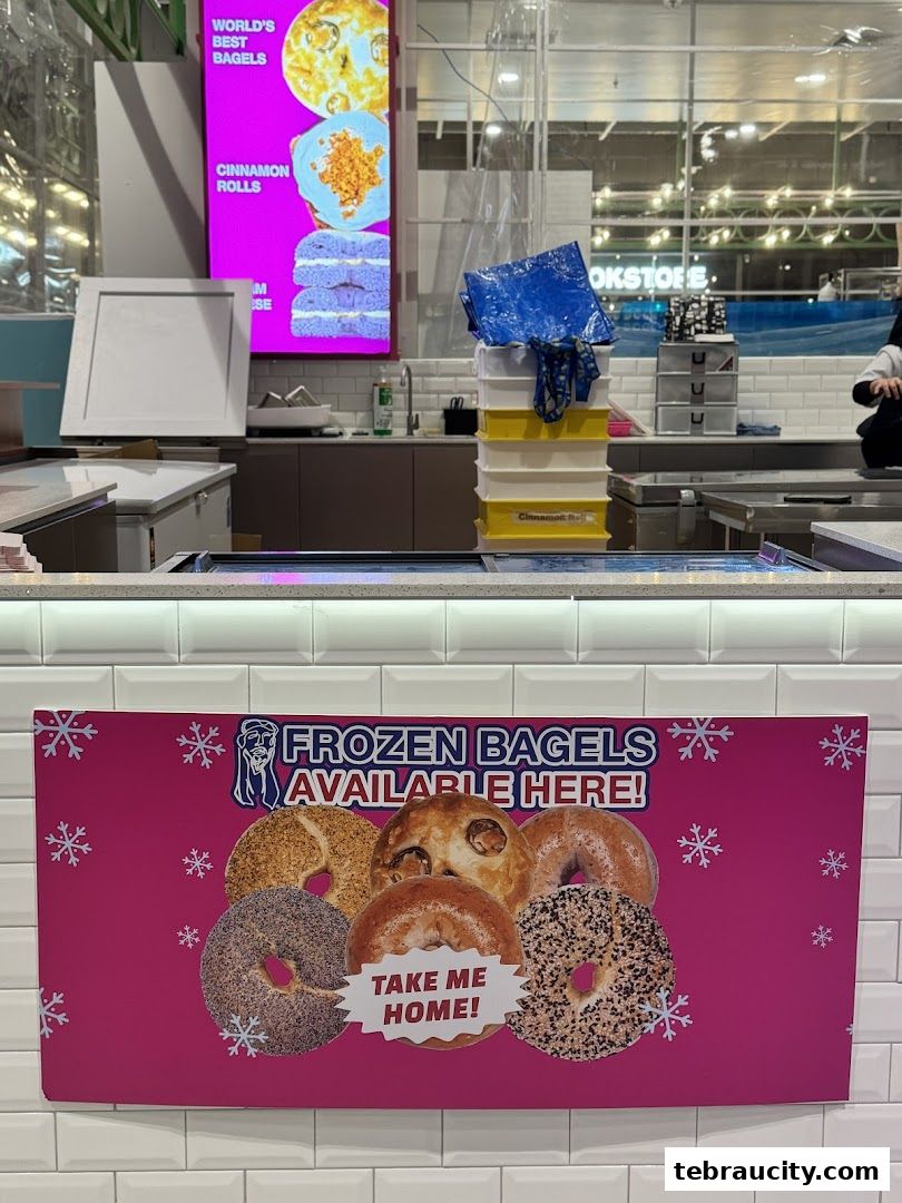 A bakery counter with a sign advertising frozen bagels and a digital display showing bagels and cinnamon rolls.