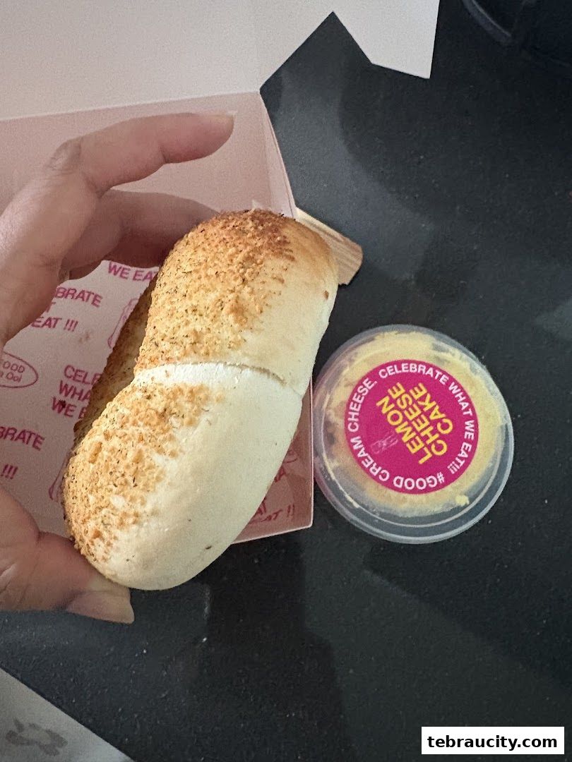 A hand holds a pastry with a small container of lemon cheese cake.