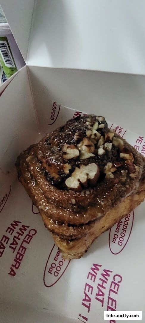 A close-up of a cinnamon roll topped with nuts and powdered sugar in a bakery box.