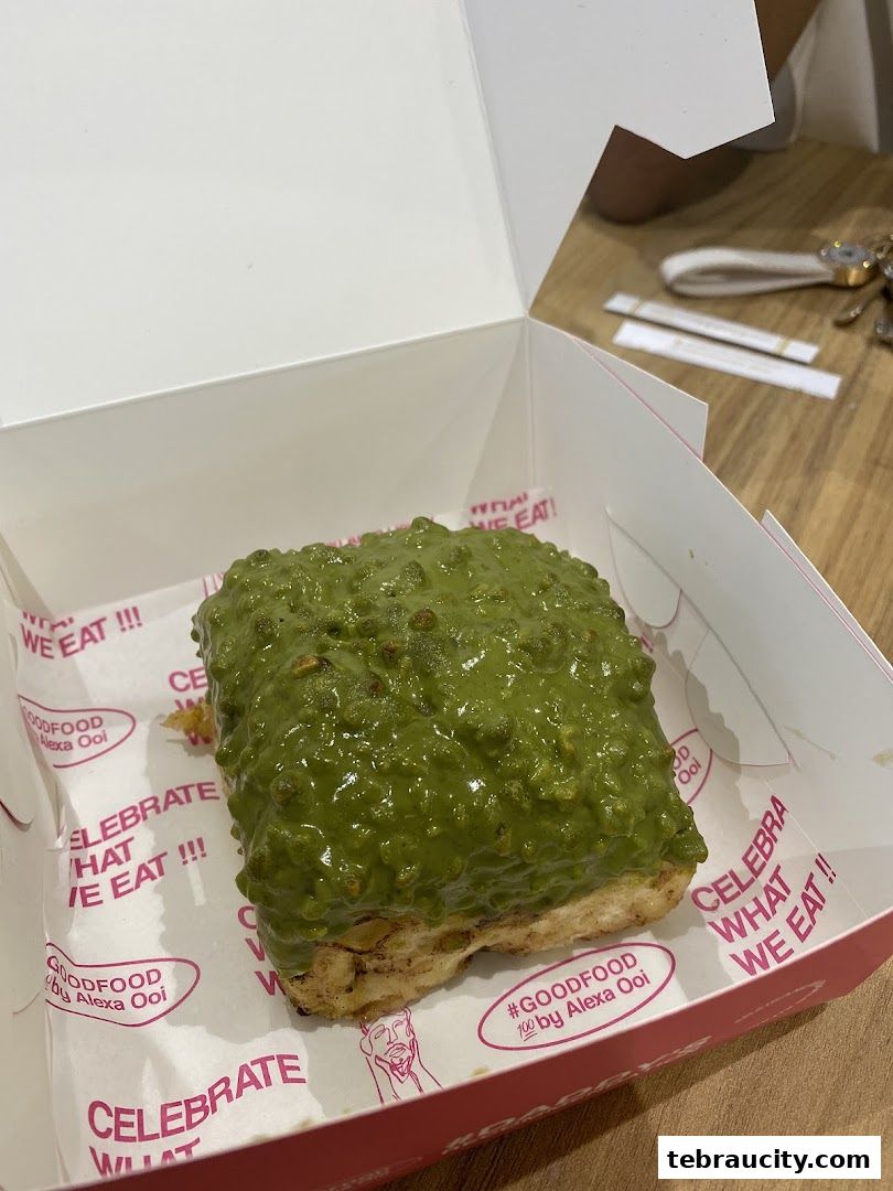 A delicious pastry with green pistachio topping in a white box.