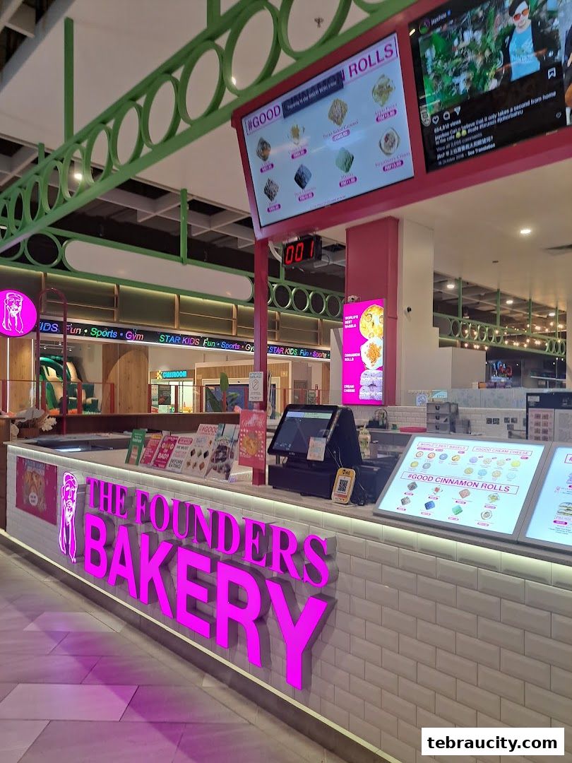 The Founders Bakery shop front with bright pink signage and digital menu boards displaying rolls.