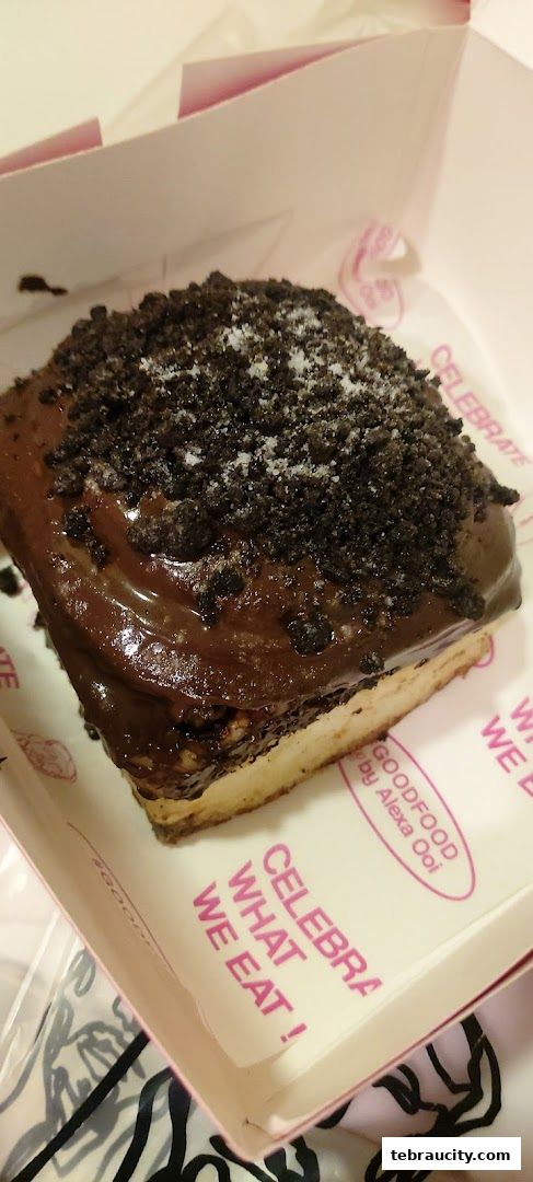 A delicious chocolate-covered pastry with cookie crumbs and sugar in a pink box.