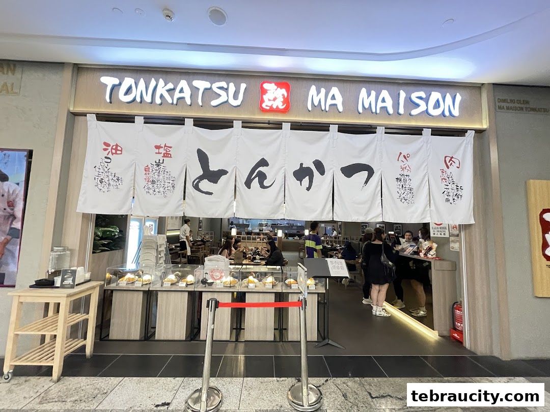 The entrance of Tonkatsu by Ma Maison restaurant with Japanese noren curtains and display cases.