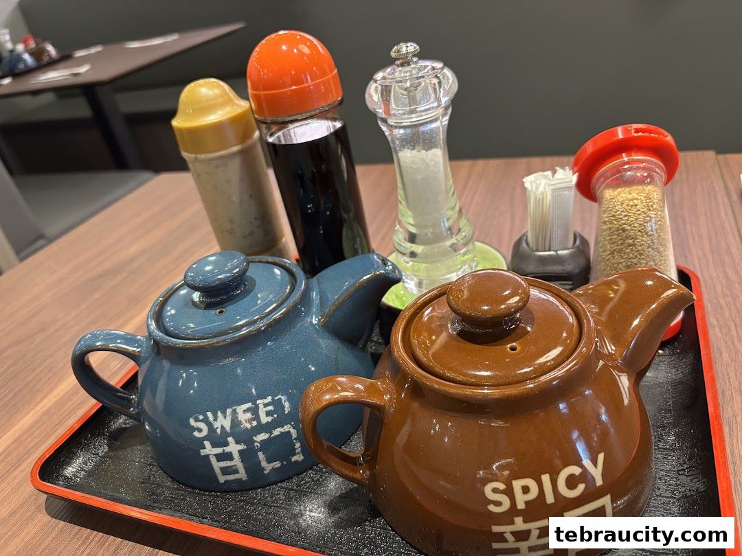 A close-up of two ceramic sauce pots, one blue and one brown, on a tray with condiments.