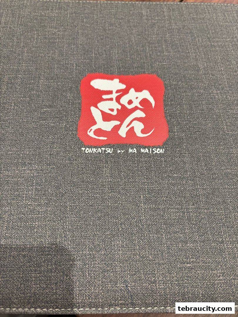 A close-up of a menu cover for Tonkatsu by Ma Maison with Japanese calligraphy.