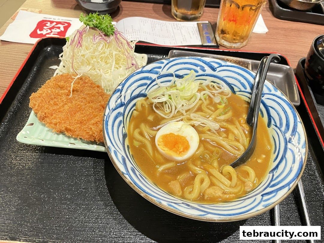 A delicious bowl of curry udon with a side of crispy fried pork cutlet and shredded cabbage.