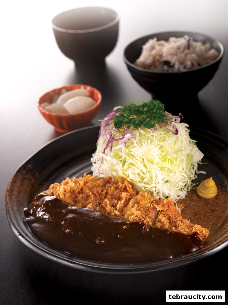 A delicious plate of Tonkatsu with curry sauce, shredded cabbage, rice, and pickles.