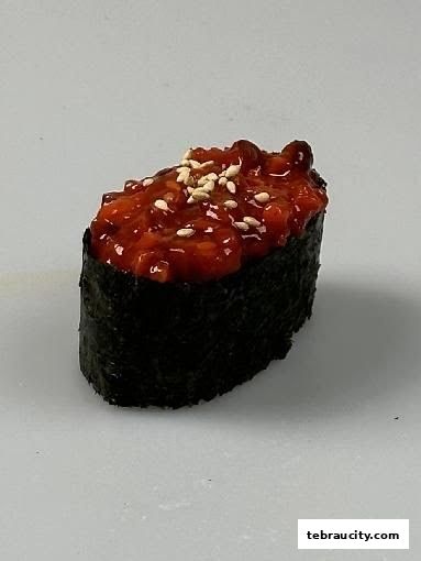 A close-up shot of a spicy tuna gunkan maki sushi roll with sesame seeds.
