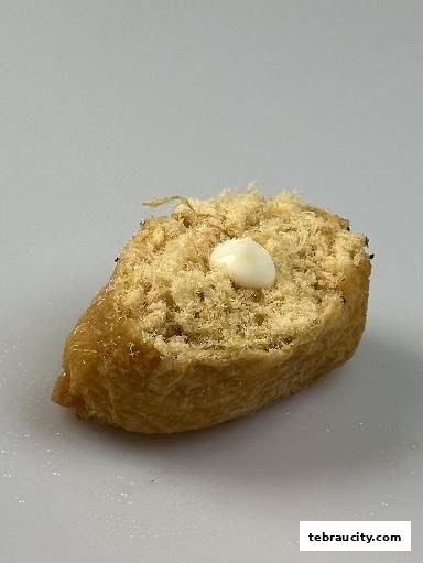 A close-up shot of a single piece of sushi with shredded meat and a dollop of mayonnaise.
