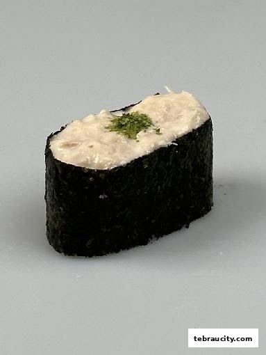 A close-up shot of a single piece of sushi with creamy filling and green garnish.