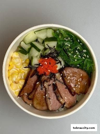 A close-up of a poke bowl with sliced duck, corn, cucumber, and seaweed salad.