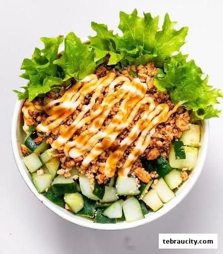 A close-up of a delicious sushi bowl with minced meat, cucumber, and lettuce, drizzled with sauce.