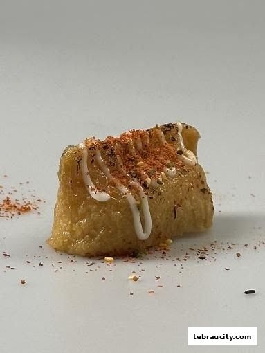 A close-up of a piece of sushi, topped with mayonnaise and spices.